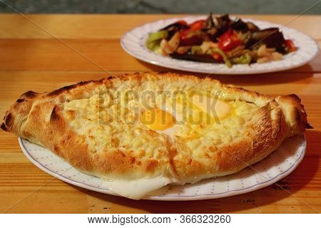 Adjaruli Khachapuri, A Traditional Georgian Cheese And Egg Bread On The Table With Blurry Eggplant S