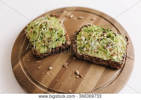 Delitious Vegan Sandwich With Guacamole And Micro Greens On Top. Half Of Avocado With Sandwich On Wo