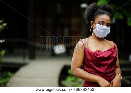 Covid-19, Infectious Virus. African Woman With Curly Hair, Wears Red Silk Dress And Medical Disposab