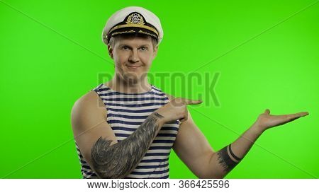 Young Muscular Sailor Man Pointing To Something With Hands. Seaman Guy Smiling In Sailors Vest. Stri