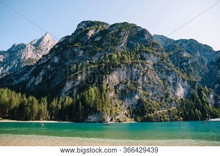 Tourists Swim In Wooden Boats On The Lago Di Braies Amid Rocky Mountains And Forests. Braies Lake In