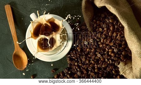 Falling sugar canes into cup of hot coffee, high angle of view. Still life scene made of pile of roasted coffee beans.