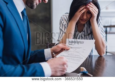 Selective Focus Of Upset Woman Covering Face Near Collector Writing In Document With Bankruptcy Lett