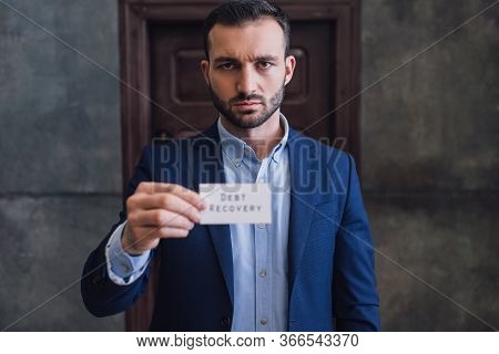 Selective Focus Of Collector Showing Card With Debt Recovery Lettering And Looking At Camera
