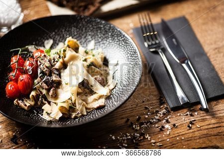 Black Angus pappardelle pasta with beef, champignon and parmegano cheese. Delicious healthy mediterranean traditional food closeup served on a table for lunch in modern cuisine gourmet restaurant