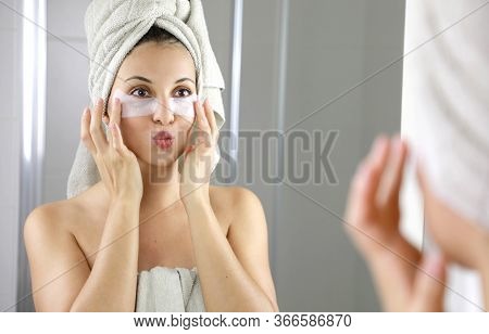 Beautiful Woman Applying Anti-fatigue Under-eye Mask Kissing Herself In The Mirror In The Bathroom. 
