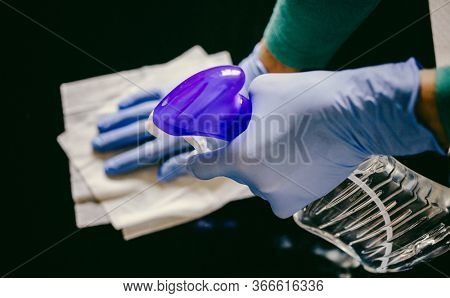 surface home cleaning spraying antibacterial sanitizing spray bottle disinfecting against COVID-19 spreading wearing medical blue gloves. Sanitize surfaces prevention in hospitals and public spaces.