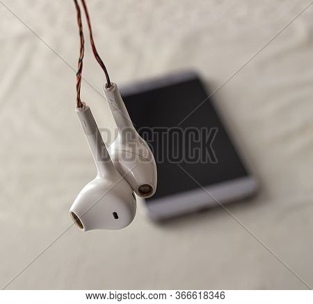 Headphones With Broken Wires. Unprotected Damaged Wires In The Background Of A Smartphone With A Bla