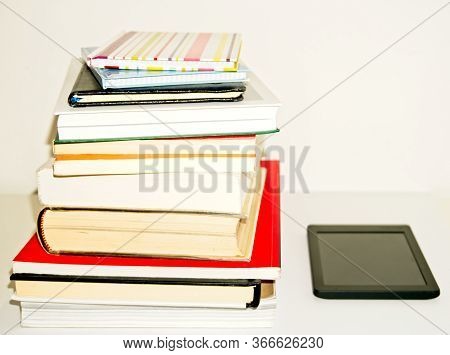 Pile Of Text Books And Books Next To An E-book On A White Background