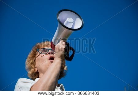 Emotional Senior Woman Makes A Speech In A Megaphone On The Outside. A Pensioner Yells Into A Sound 