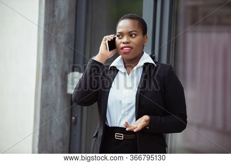 Talking On Phone. African-american Businesswoman In Office Attire Smiling, Looks Confident And Happy