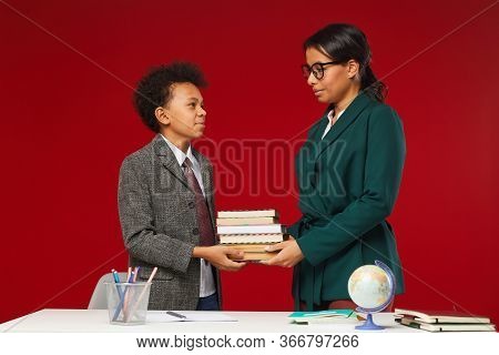 Side View Portrait Of Young Female Teacher Giving Books To Cute African-american Boy In School, Scen