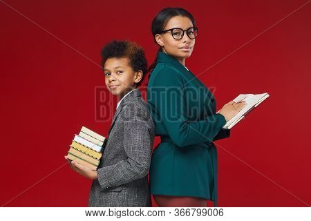 Waist Up Portrait Of Female Teacher And Cute African-american Boy Standing Back To Back Holding Book