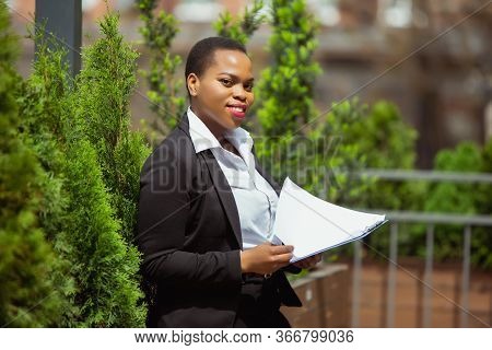 Paperwork. African-american Businesswoman In Office Attire Smiling, Looks Confident And Happy, Busy.