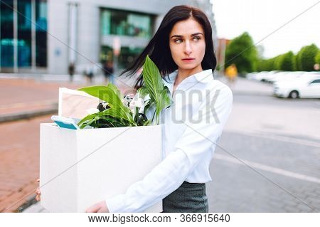 Young Sad Business Woman In Office Siut With A Box Of Her Office Supplies With Buisness Center At Ba