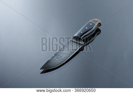 An All-metal, Middle Kitchen Knife Lies On A Mirror Surface, A Blade Made Of Multilayer Damask Steel
