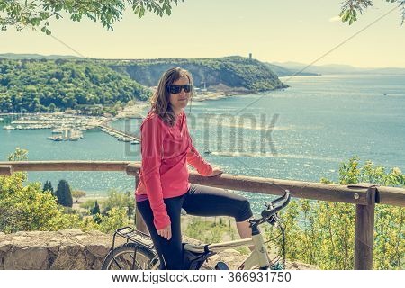Active Female Cyclist Taking A Rest On Her Bike And Enjoying Amazing Sea View.