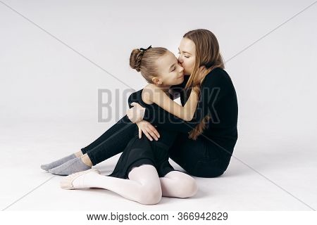 Mother Encourages Her Daughter Ballerina Sitting On The Floor On White Background.