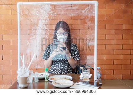 Asian Woman Using Smartphone During Dining Time In Restaurant With Separated Of Shield Plastic Parti
