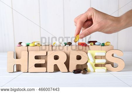 Woman Putting Pill Near Word Herpes On White Wooden Table, Closeup