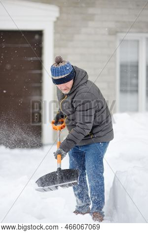 Mature Man Clean Path Near House From Snow During Strong Blizzard. Person Shoveling Snow Out Of Driv