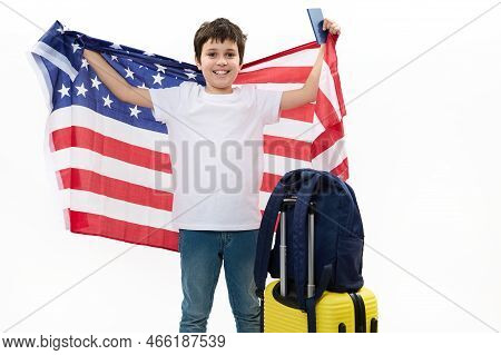 Happy Preteen Boy In White T-shirt And Blue Jeans, Holds Usa Flag And Boarding Pass, Smiles At Camer