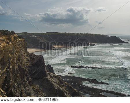 View Of Praia De Odeceixe Mar Beach With Ocean Waves, Cliffs And Stones, Wet Golden Sand And Green V