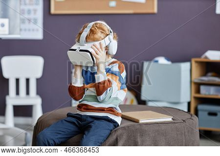 Gingerhaired Little Boy In Striped Pullover And Vr Headset Playing Virtual Game While Sitting On Rou