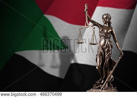 Sudan Flag With Statue Of Lady Justice And Judicial Scales In Dark Room. Concept Of Judgement And Pu