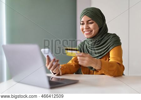 Online Payments. Muslim Woman Using Smartphone And Credit Card At Home Office