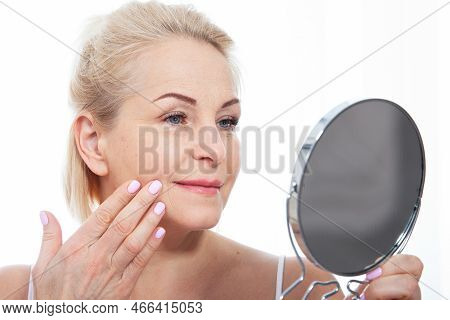 Happy Middle Aged Woman Model Touching Face Skin Looking In Mirror. Smiling Mature Older Lady Enjoyi