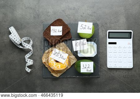 Calculator And Food Products With Calorific Value Tags On Dark Grey Table, Flat Lay. Weight Loss Con
