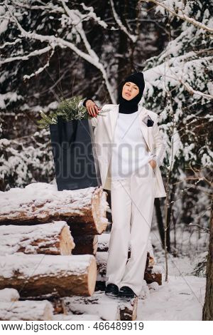 A Girl In A White Suit And Balaclava With A Package Of Christmas Trees In The Winter Forest On New Y