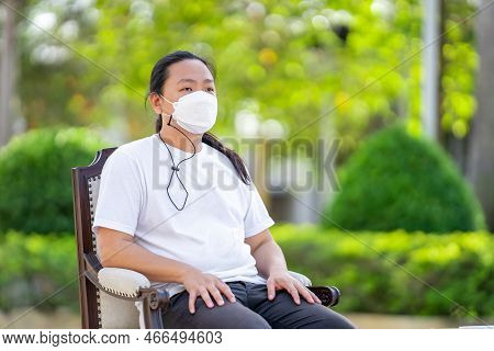 A Man Wearing White T Shirt And White Mask Is Sitting Calm On The Armchair With His Arms On The Armr