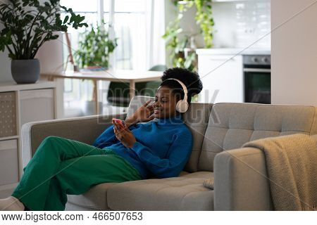 Happy African American Woman In Headphones Listening To Music Using Mobile Phone To Select Playlist 