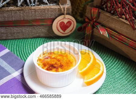 Portion Of Dessert Crème Brûlée With Caramel Crust In Ramekin With Orange Slices On A Plate