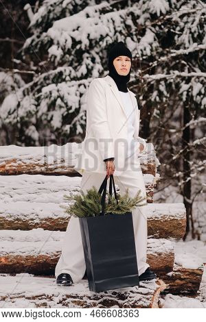 A Girl In A White Suit And Balaclava With A Package Of Christmas Trees In The Winter Forest On New Y