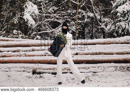 A Girl In A White Suit And Balaclava With A Package Of Christmas Trees In The Winter Forest On New Y