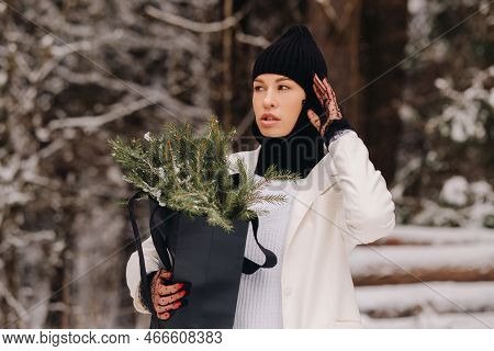 A Girl In A White Suit And Balaclava With A Package Of Christmas Trees In The Winter Forest On New Y