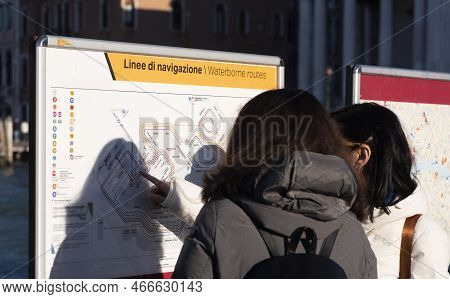 Two Female Tourists Read The Navigation Map While Choosing Route Options In Venice, Italy . Text: 