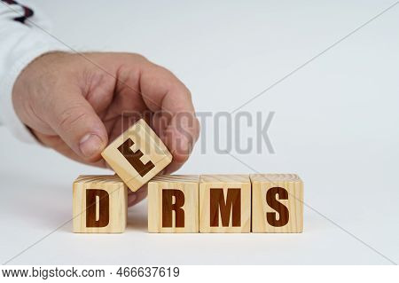 Business Concept. On A White Surface, A Man Stacks Cubes With The Inscription - Derms