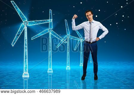 Young Businessman Flexing Muscle And Looking At Glowing Digital Wind Mill Turbine Hologram On Blue B