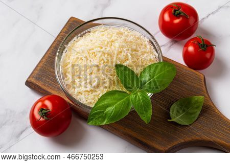 Bowl Of Grated Parmesan And Tomatoes Over Marble Surface. Shredded Grana Padano Cheese In A Glass Bo
