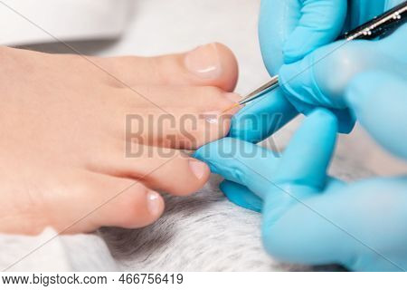 A Pedicure Master In Medical Gloves Takes Care Of Beautiful Female Toenails. Close-up. The Concept O