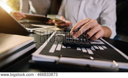Business Documents On Office Table With Smart Phone And Laptop And Two Colleagues Discussing Data In