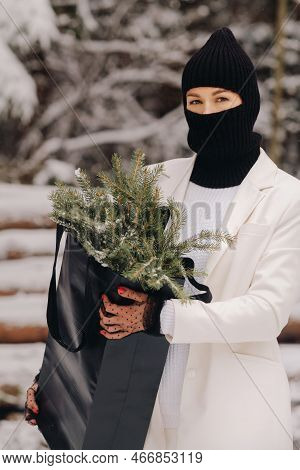 A Girl In A White Suit And Balaclava With A Package Of Christmas Trees In The Winter Forest On New Y