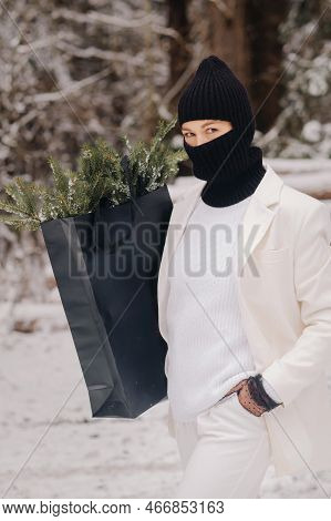 A Girl In A White Suit And Balaclava With A Package Of Christmas Trees In The Winter Forest On New Y