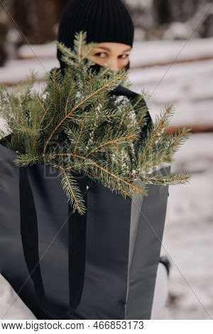 A Girl In A White Suit And Balaclava With A Package Of Christmas Trees In The Winter Forest On New Y