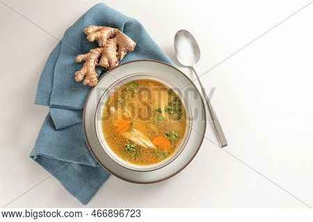Healthy Soup From Chicken Meat, Vegetables And Ginger In A Bowl On A Blue Napkin And A Gay White Bac
