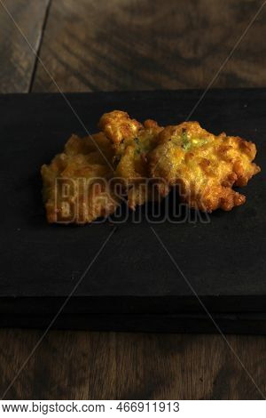 Bakwan Jagung Or Corn Fritters Is On A Black Cutting Board Against A Wooden Background